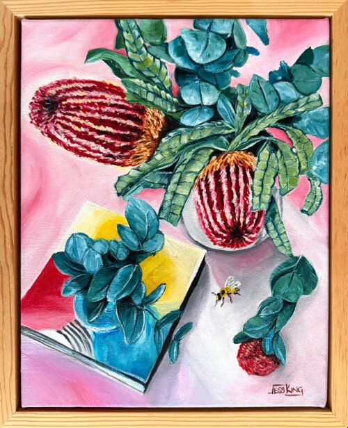 "Banksia and Bees" is an original oil painting by Australian artist Jess King, featuring banksia flowers, a trailing jade plant in a blue vase, a bumblebee, and an open book against a pink background.